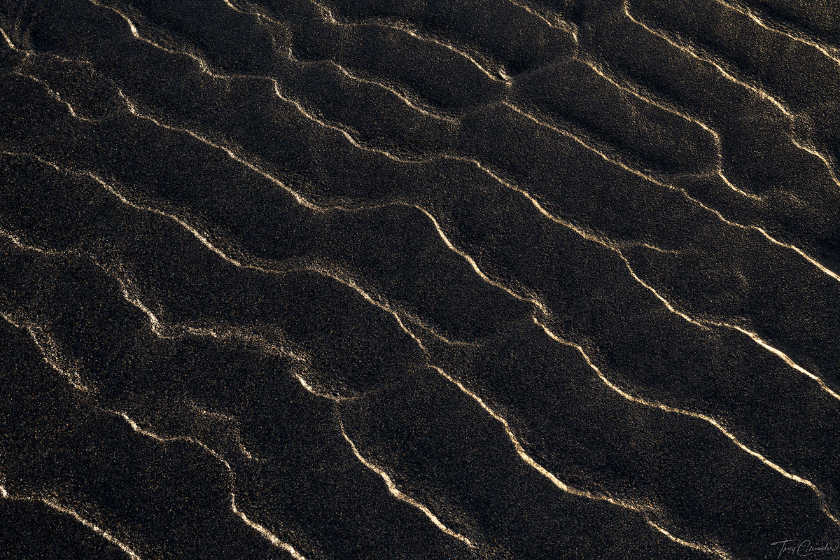 First kiss of light upon small ripples in black sand.