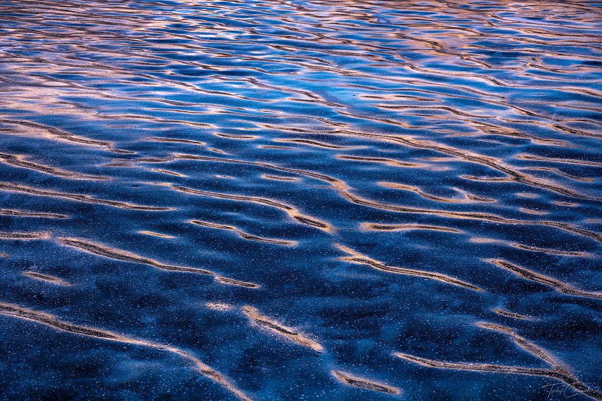 Sunrise alpenglow reflected on the tips of ripples in ice on a frozen lake.